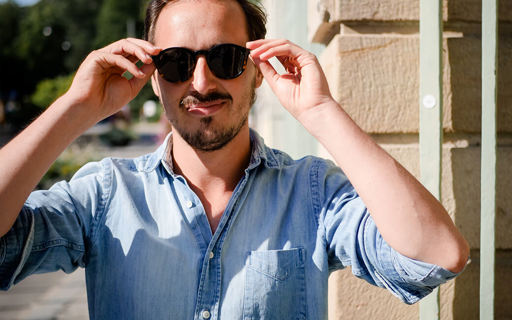 Clement står på ett gathörn i stark sol. Han har kort mörkt hår och ser cool ut i solglasögon och jeansskjorta.